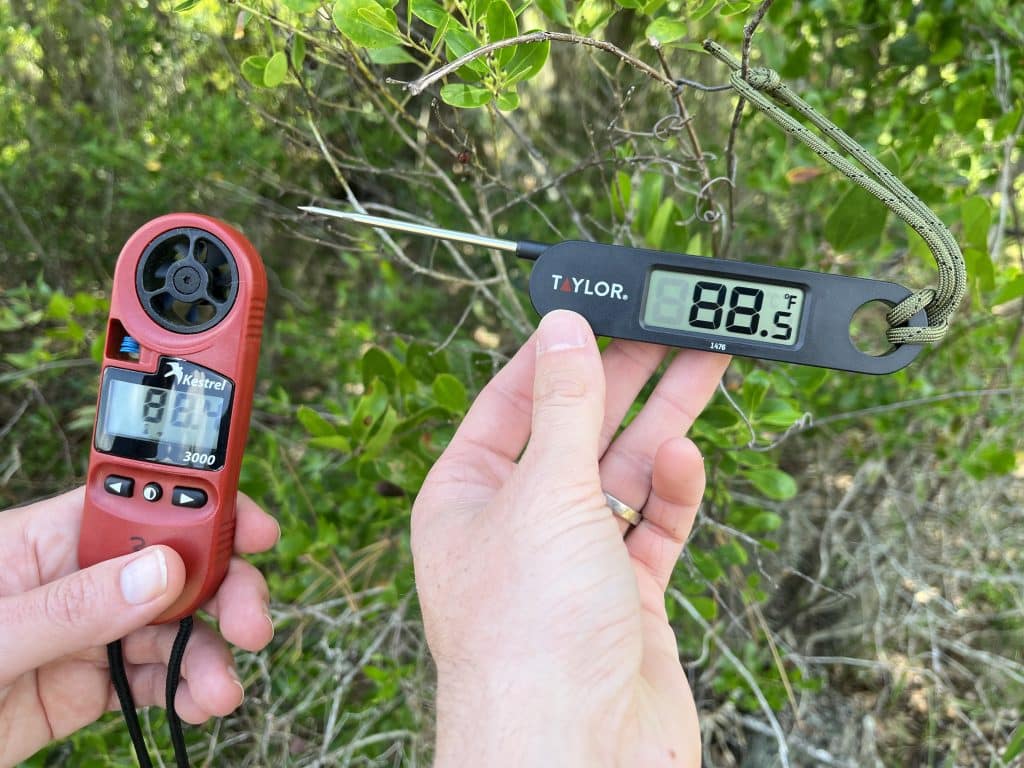 Two different types of digital thermometer are held up by two hands. One thermometer is a Kestrel weather meter, while the other is a Taylor cooking thermometer. The Kestrel reads 88.4 degrees Fahrenheit and the Taylor thermometer reads 88.5 degrees Fahrenheit.